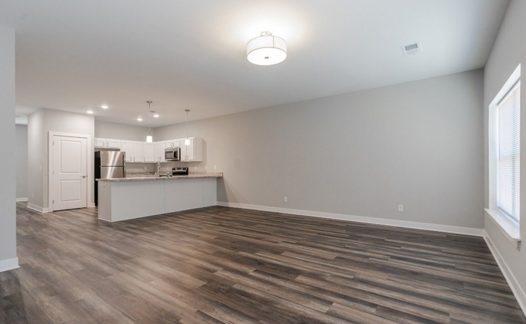 A room with wooden flooring and a kitchenette in the background.