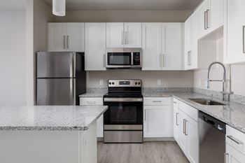 A kitchen with a refrigerator, microwave, oven, and sink.
