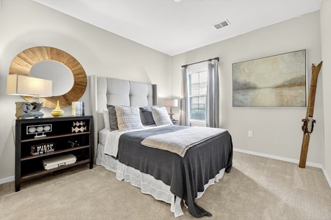 A bedroom with a bed, nightstand, and a painting on the wall.