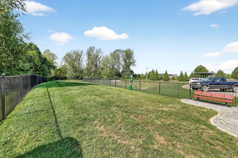 A black fence surrounds a grassy area with a car and truck parked on the right side.