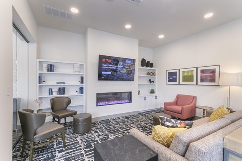 A living room with a grey sofa, a red chair, a black and white rug and a TV on the wall.