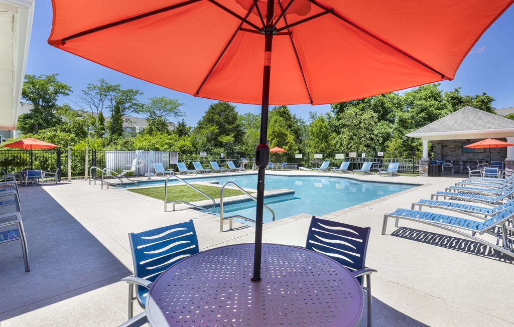 our apartments have a pool and patio with chairs and an umbrella at Aventura at Towne Centre, Missouri, 63011