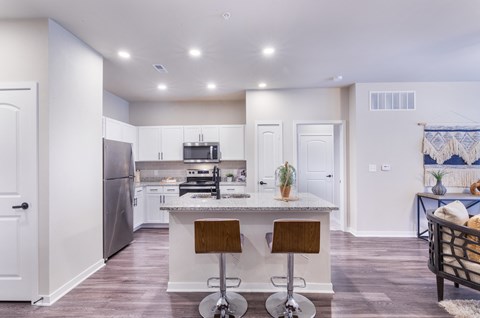 a kitchen with white cabinets and a counter top with three stools at Aventura at Wild Horse Creek, Chesterfield, 63017