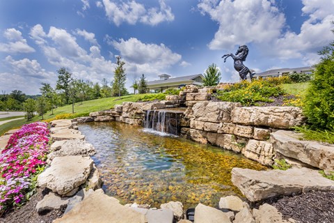 a pond with a waterfall and a statue on a hill at Aventura at Wild Horse Creek, Chesterfield