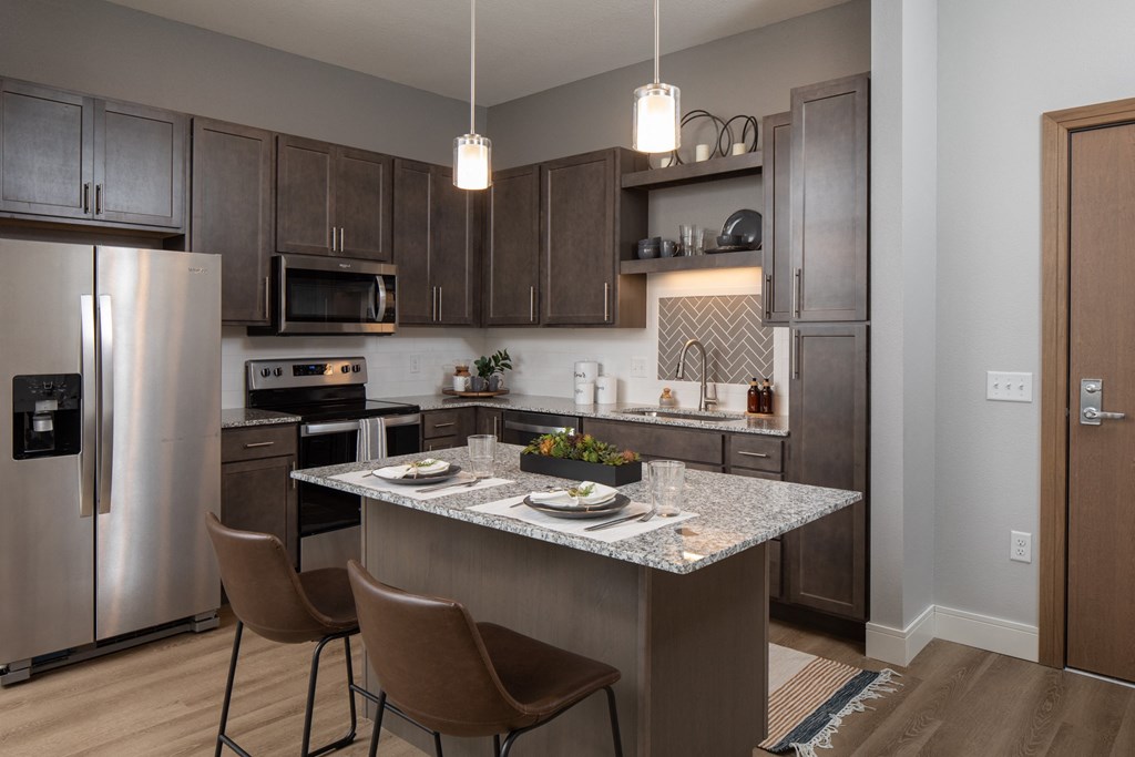 a kitchen with a large island with granite countertops and stainless steel appliances at The Edison at Rice Creek, Shoreview, MN
