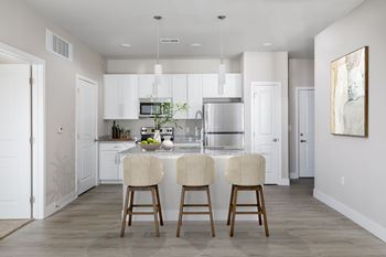 A kitchen with white cabinets and a center island with two chairs.