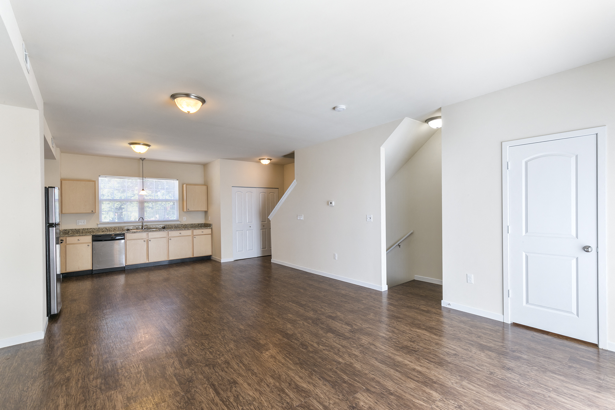 an empty living room and kitchen with wood flooring and white walls
