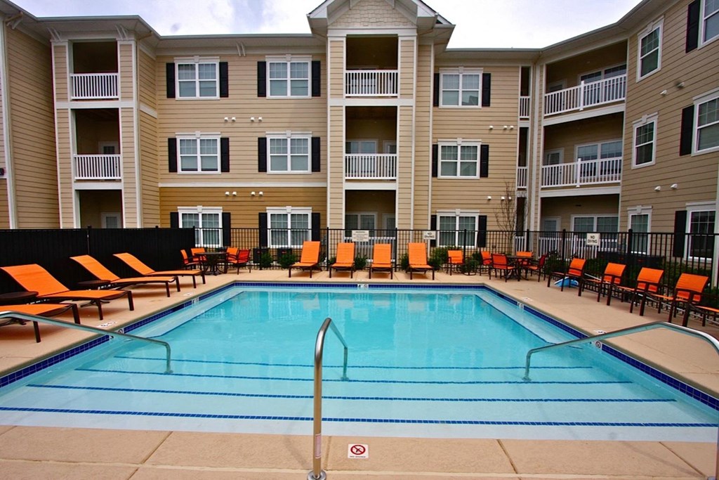 a swimming pool in front of an apartment building with orange chairs