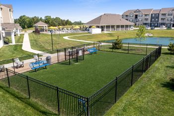 A black fence surrounds a green lawn with a pool and a playground at Aventura at Wentzville I & II Apartments, Missouri