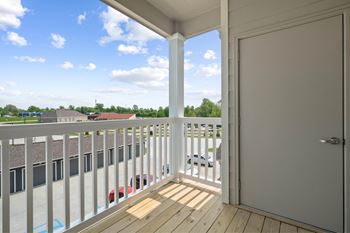 A balcony with a white door and a red car parked in the parking lot at Aventura at Wentzville I & II Apartments, Wentzville, MO