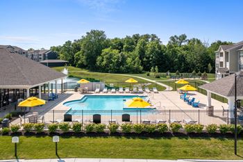 A large swimming pool surrounded by yellow umbrellas and blue loungers at Aventura at Wentzville I & II Apartments, Wentzville, MO, 63385