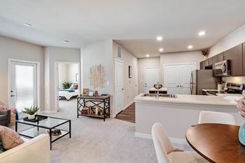 A modern living room with a white sofa, a glass coffee table, and a dining area with a white table and chairs at Aventura at Wentzville I & II Apartments, Wentzville, MO, 63385