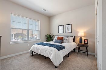 A bedroom with a bed, nightstand, and two framed pictures on the wall at Aventura at Wentzville I & II Apartments, Wentzville, MO