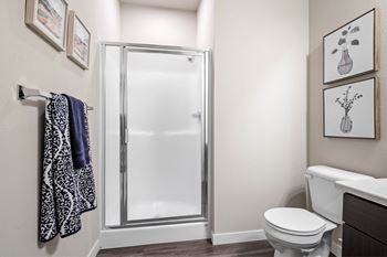 A bathroom with a toilet, a shower with a glass door, and towels hanging on a rack at Aventura at Wentzville I & II Apartments, Missouri