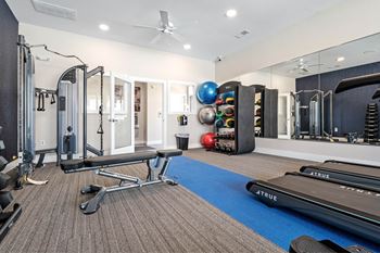 A well equipped gym with a mirrored wall and a variety of exercise equipment at Aventura at Wentzville I & II Apartments, Wentzville
