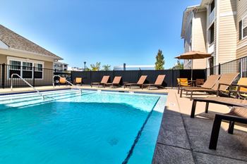 A swimming pool with sun loungers and a building in the background.