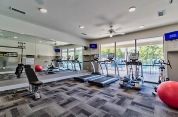 A gym with treadmills, elliptical machines, and exercise balls.