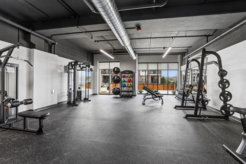 A gym with a variety of equipment including dumbbells, weight plates, and benches.