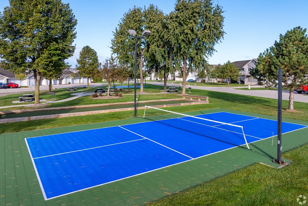 A blue tennis court surrounded by trees and grass.