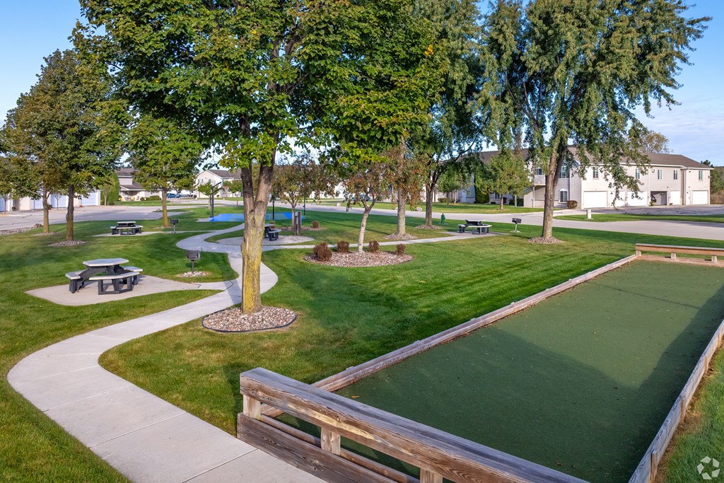 A green lawn with a small putting green and a wooden fence.