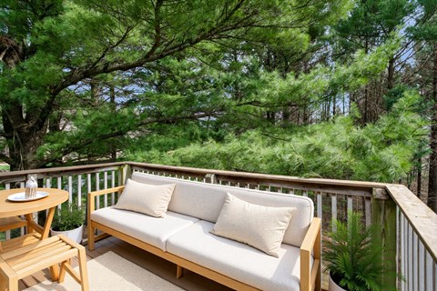 A wooden bench with cushions is on a balcony with a table and chairs.