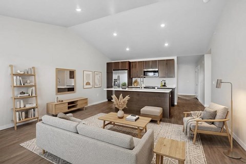 A modern living room with a grey sofa, wooden coffee table, and a kitchen area in the background.