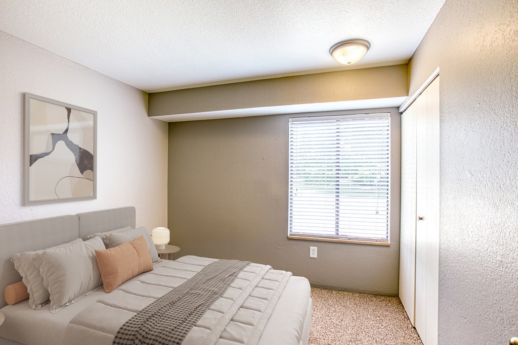 A bedroom with a bed, pillows, a nightstand, and a window with blinds.