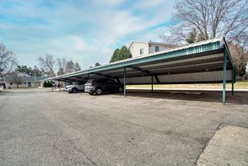 A car is parked under a green metal awning in a parking lot.