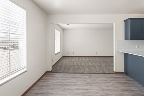 A spacious room with a grey carpet and a window with blinds.