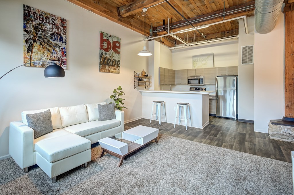 A white couch with grey pillows sits in a room with a wooden ceiling and a framed poster on the wall.