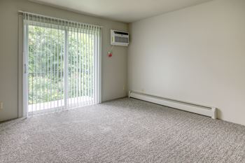 A room with a window, a wall-mounted air conditioner, and a carpeted floor.