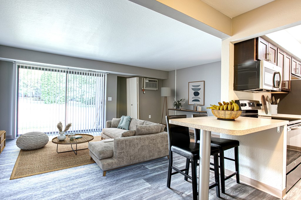 A modern kitchen with a dining table and chairs is adjacent to a living room with a couch and a coffee table.