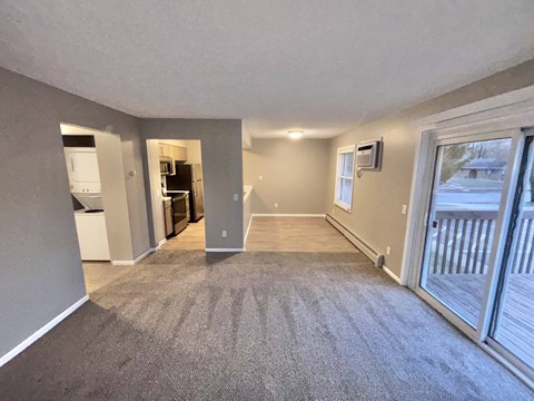 A spacious living room with a grey carpet and a sliding glass door leading to a deck.