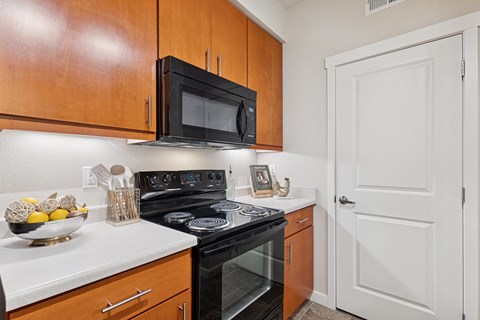 A kitchen with a black microwave above a stove and wooden cabinets.