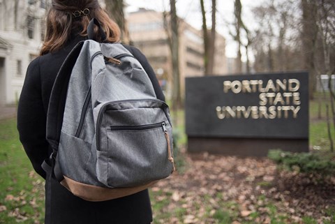 a woman with a backpack standing in front of the fountain state university sign