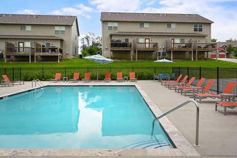 A swimming pool surrounded by red chairs and apartment buildings in the background.