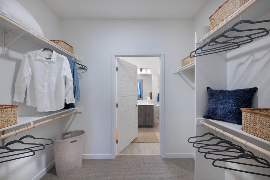 a walk in closet with white closets and a door to a bathroom