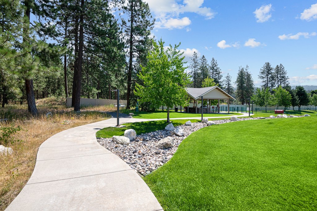 a sidewalk leading to a park with a gazebo and trees