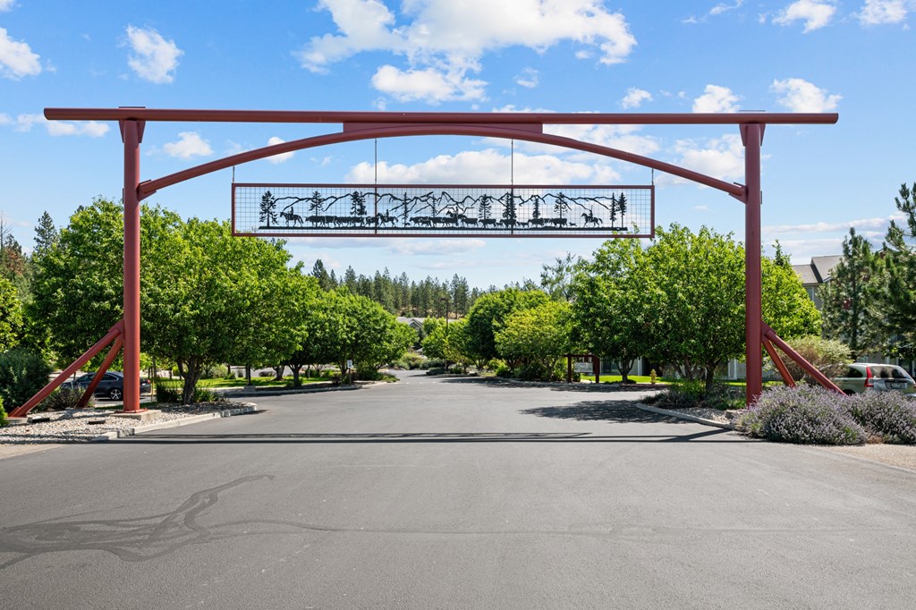 the arch at the end of a road with trees and a driveway