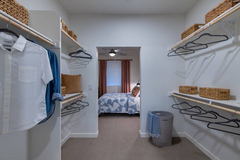 a walk in closet with shelves and racks and a bedroom with a bed
