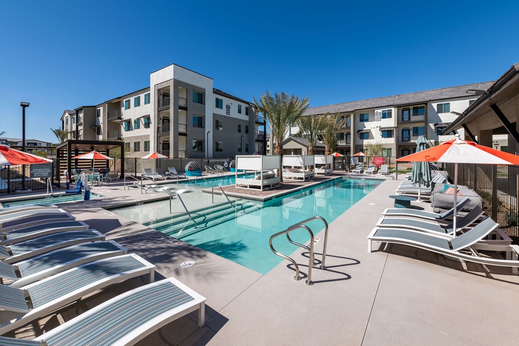 a pool with lounge chairs and umbrellas in front of an apartment building