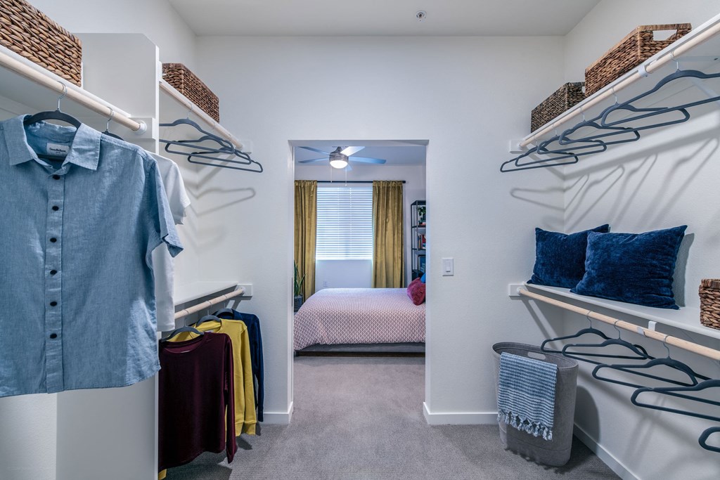 a walk in closet with a bedroom in the background and shelves with clothes on them