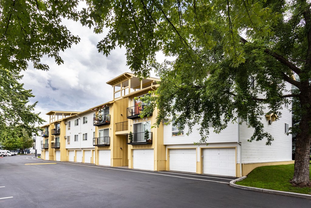 a street view of a building with white and yellow siding and a tree in the foreground