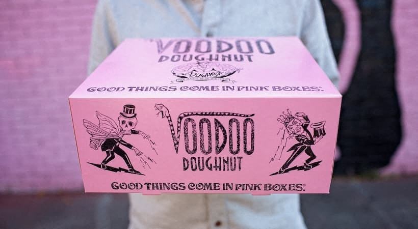 a person holding a pink box that says voodoo doughnut