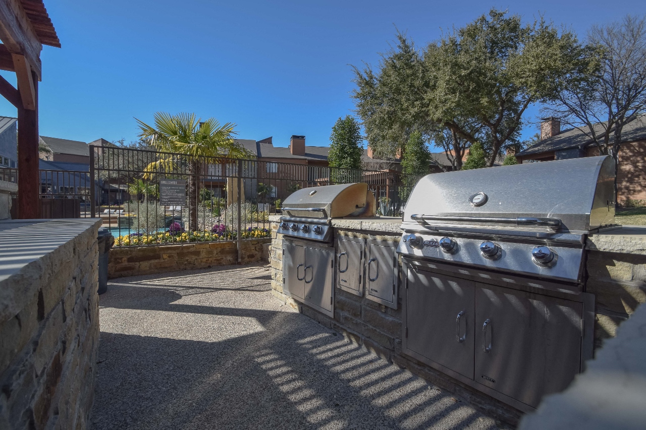 two stainless steel barbecue grills in an outdoor area with trees