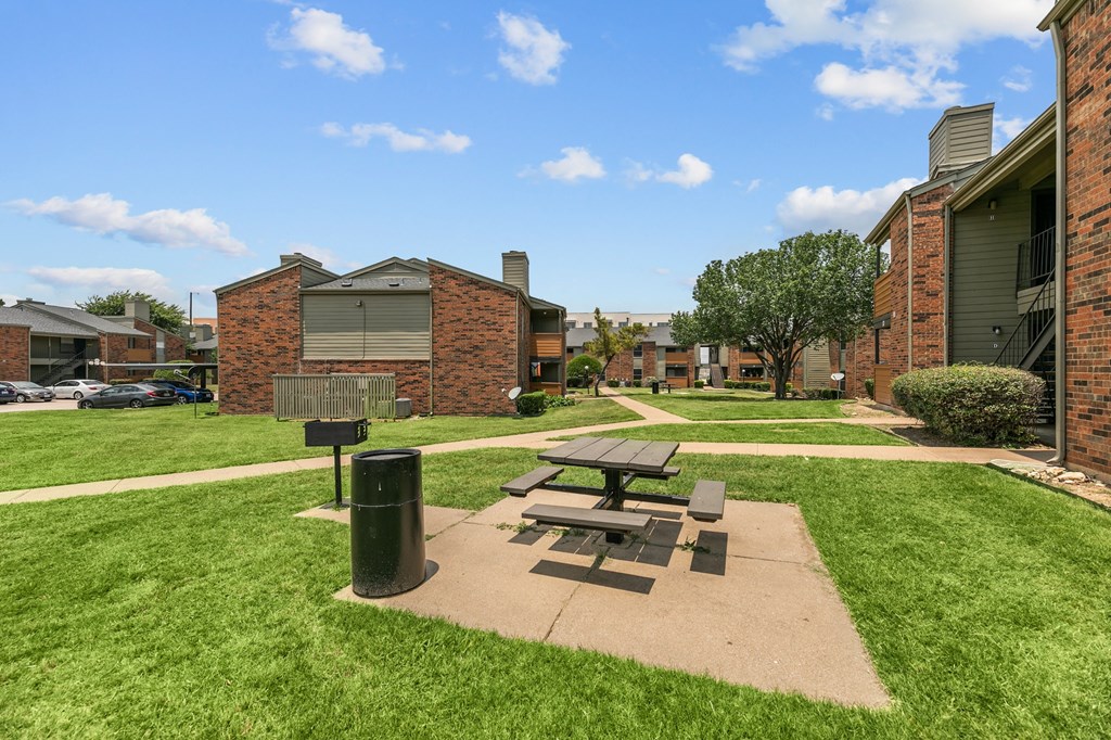 a picnic table and grill sit in a grassy area in front of a brick building at The Hills at Ironhorse, North Richland Hills, TX, 76180