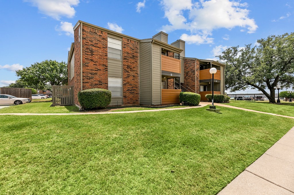 an apartment building with a green lawn and trees in the background at The Hills at Ironhorse, North Richland Hills, 76180