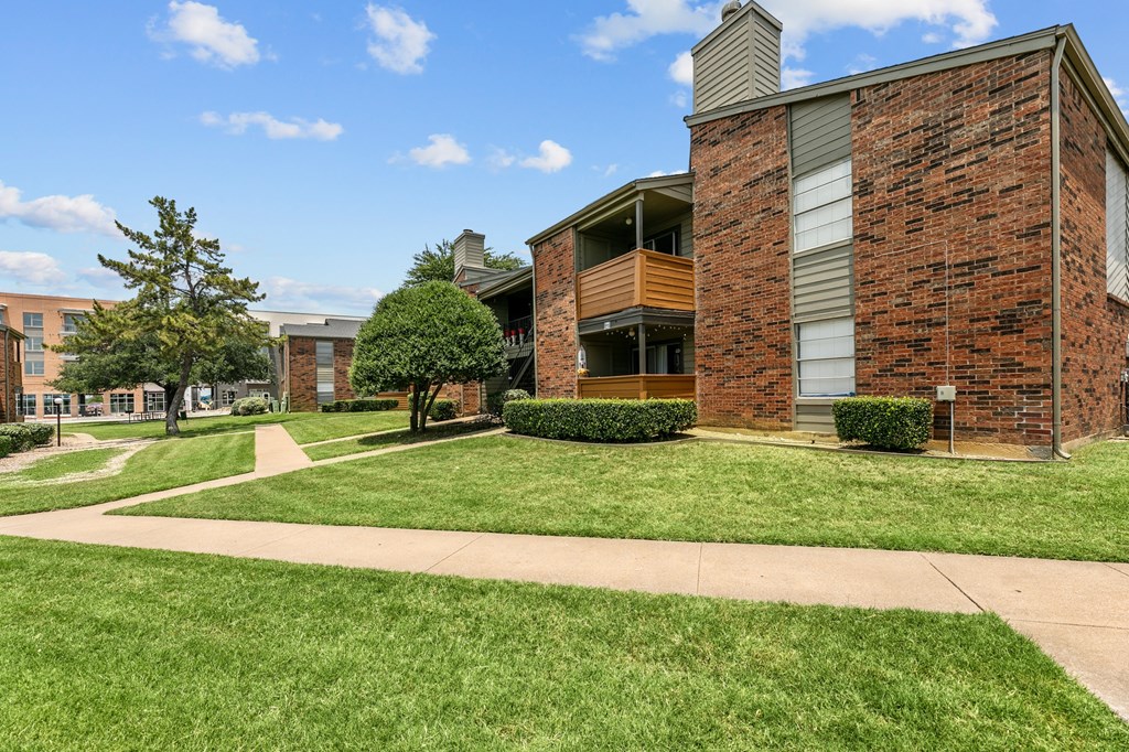 a grassy area with trees and bushes in front of a brick building at The Hills at Ironhorse, Texas