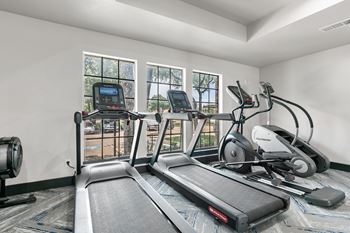 A treadmill, elliptical trainer, and stationary bike are in a room with large windows.