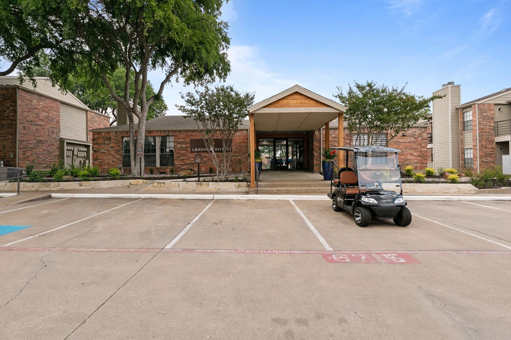 a golf cart sits in a parking lot in front of a brick building at The Hudson, Texas, 76180